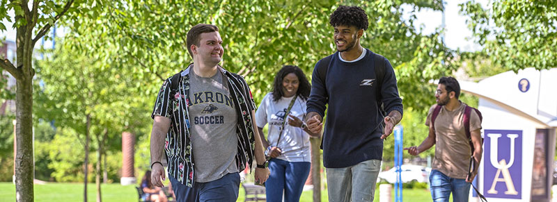Four students walk on campus while discussing The University of Akron admissions process.