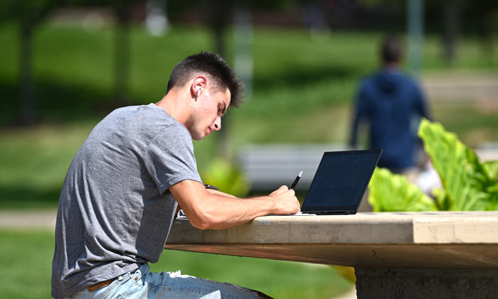 A student with his laptop studying at a table outdoors in Coleman Common