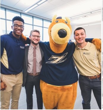 Three College of Business students standing arm in arm with Zippy the mascot.