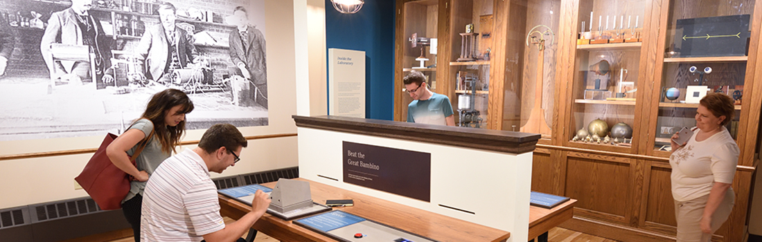 Museum visitors gathered around an interactive display. Two are interacting with the display and two others are watching from a short distance