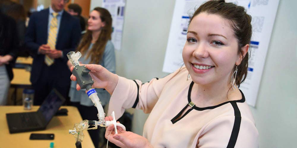 A biomedical engineering student at a conference shows off a device she designed.