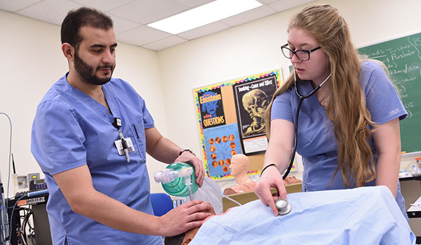 Two nursing students work together in a lab to assist a patient.
