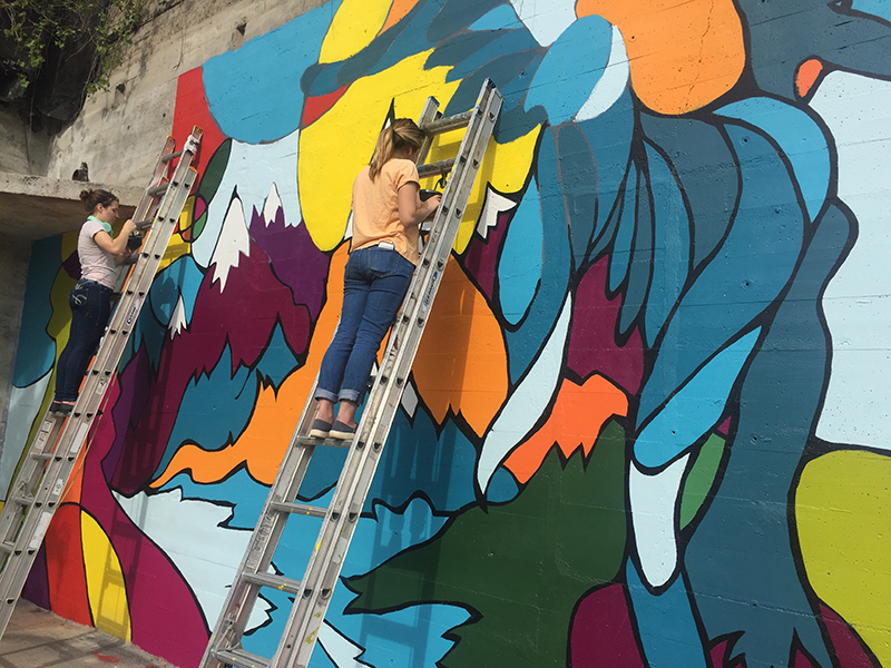 students on ladders painting mural