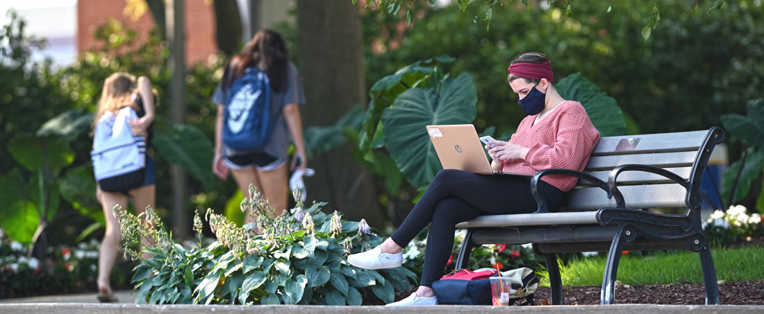 A student with her laptop is studying on a bench near the library