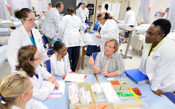 Nursing students in a lab listen to instructions from a faculty member